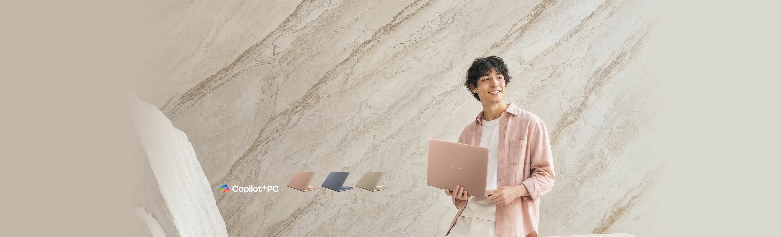 Person standing against a marble-textured wall holding a Komodo Coral ASUS Zenbook 14 laptop, showcasing its lightweight, stylish design in a bright modern setting.